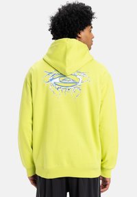 Bright yellow hoodie with a hood, featuring a stylized blue logo surrounded by crack designs on the back. Soft fabric texture.