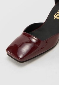 Pantofii din piele lacuită cărămizie, cu un design cu vârf pătrat, laturi tăiate joase și o branț texturat negru. Talpă plată cu finisaj neted.