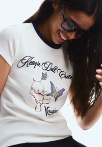 White cotton t-shirt with navy collar, featuring a cartoon character and butterflies in pastel colors. Design includes stylized text.