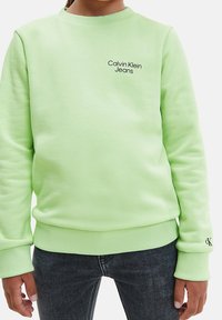 Světle zelená mikina z měkké látky, s žebrovanými manžetami a lemem. Na hrudi černé logo „Calvin Klein Jeans“, minimalistický design.