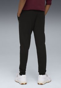 Svarta sweatpants i mjukt tyg med sidofickor, elastiska mudd och en diskret logodetalj nära midjan. Samt en vit sneakers.