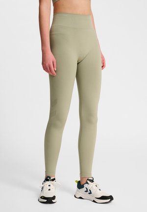Helle grüne Leggings mit einem hohen Bund, aus einem glatten Material. Sie verfügen über ein dezentes Muster an der Seite und sind mit weißen Sneakers kombiniert.