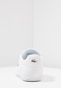 Baskets blanches en matériau synthétique lisse, design bas, bout arrondi, et semelle en caoutchouc texturée. Présente une étiquette logo sur le talon.