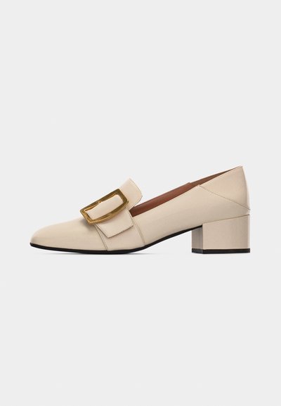 Chaussure beige en cuir à talon bas avec bout pointu et grande boucle dorée latérale, vue de profil sur fond blanc.