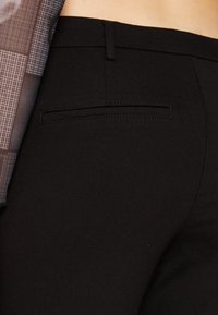 Pantaloni negri croiți, cu o textură netedă, curea pentru brâu, un buzunar la spate și un design ajustat, completate de un top cu un model.