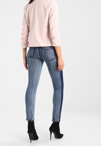 Slim fit jeans w kolorze średniego niebieskiego denimu z bocznymi paskami, zestawione z dopasowanym jasnoróżowym żakietem i botkami za kostkę. Szczegół z postrzępionym dołem.
