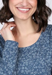 Blaues Oberteil mit Blumenmuster, Rundhalsausschnitt, langen Ärmeln und weicher Stofftextur, das hellblaue Blumen auf einem dunkelblauen Hintergrund zeigt.