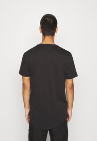 T-shirt in cotone nero con maniche corte e colletto rotondo. Presenta un orlo curvo e un design semplice. La vista posteriore non mostra grafiche.