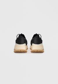Scarpe sportive nere con materiale liscio, design arrotondato, suole chiare e struttura minimalista con linguetta sul tallone.