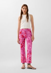 Witte geribde mouwloze top gecombineerd met roze tie-dye wijde jeans met rode en blauwe accenten en stiksel langs de tailleband.