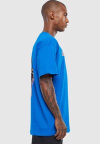 Blå bomulds t-shirt med korte ærmer, prydet med et grafiktryk på ryggen. Rund halsudskæring og afslappet pasform.