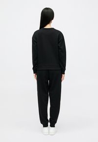 Μαύρο φού�τερ και ταιριαστά παντελόνια φόρμας, κατασκευασμένα από μαλακό υλικό. Διαθέτει στρογγυλή λαιμόκοψη, μακριά μανίκια και ελαστικές μανσέτες και μέση.