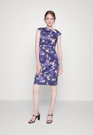Vestido floral roxo com mangas curtas, forma ajustada e comprimento até o joelho. Apresenta flores vibrantes multicoloridas com uma textura semelhante a cetim. Sapatilhas pretas.