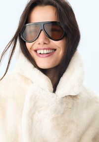Faux fur cremefarvet jakke med hætte og blød tekstur. Store sorte solbriller med rund form og brune linser. Generelt afslappet og moderne look.