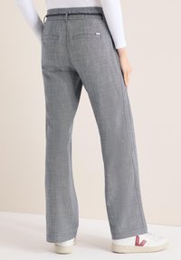 Pantalon large gris en tissu texturé, avec une poche arrière et une ceinture, associé à des baskets blanches avec des accents roses.