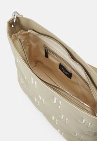 Sac à main beige avec motif de logo en relief, fermeture éclair argentée et doublure intérieure douce. Comprend un compartiment principal et une petite poche intérieure.