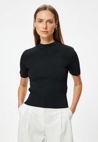 Top negro de manga corta con textura, cuello alto y forma ajustada, combinado con pantalones blancos con pliegues.