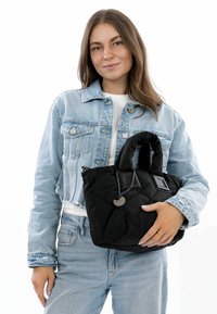 Borsa a tracolla nera trapuntata con manici doppi, caratterizzata da dettagli argentati e una finitura testurizzata, tenuta da una persona che indossa una giacca di denim.