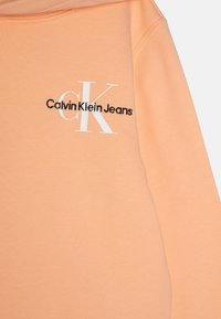 Felpa con cappuccio color pesca di Calvin Klein con logo bianco. Presenta una texture morbida, una vestibilità standard e un design minimalista.