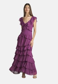 Lila gestufte Maxikleid mit Rüschensäumen und tiefem V-Ausschnitt. Hergestellt aus leichtem Stoff, mit fließenden Lagen und einem taillierten Oberteil.