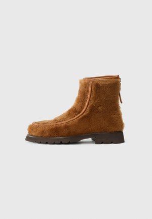Botas de tobillo de piel de oveja marrones con un acabado texturizado, que cuentan con un cierre de cremallera y una suela de goma resistente.