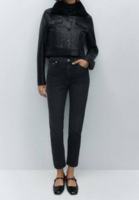 Czarna skórzana kurtka z krótkim krojem i futrzanym kołnierzem, zestawiona z czarnymi dżinsami z wysokim stanem oraz błyszczącymi czarnymi balerinami z kokardą.