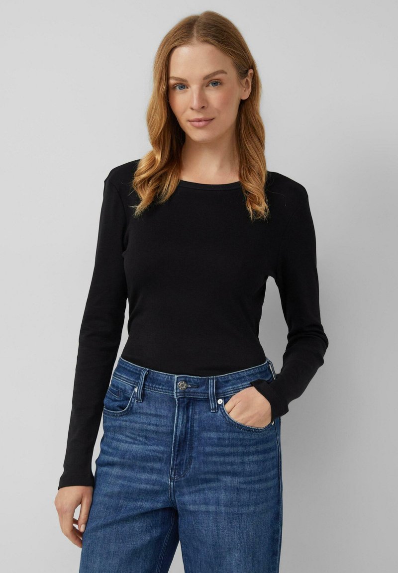 Maglietta nera a maniche lunghe con scollatura rotonda, abbinata a jeans a vita alta blu. Il tessuto sembra morbido con una silhouette aderente.