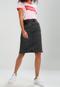 Svart denimpencilkjol med hög midja, med en framsöm och smal passform, kombinerad med en rosa t-shirt med Levi's-logotyp och vita sneakers.