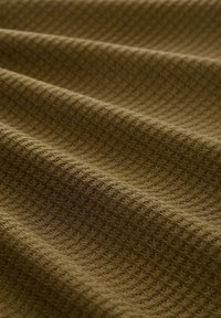 Olivgrüner, strukturierter Stoff mit einem Rautenmuster, weich mit sichtbaren Rillen, in Wellen gefaltet, was die Tiefe und Oberfläche des Materials betont.