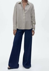 Chemise à rayures crème et noir avec manches longues, associée à un pantalon en denim bleu foncé à jambes larges. Comprend un col et des boutons à l'avant.