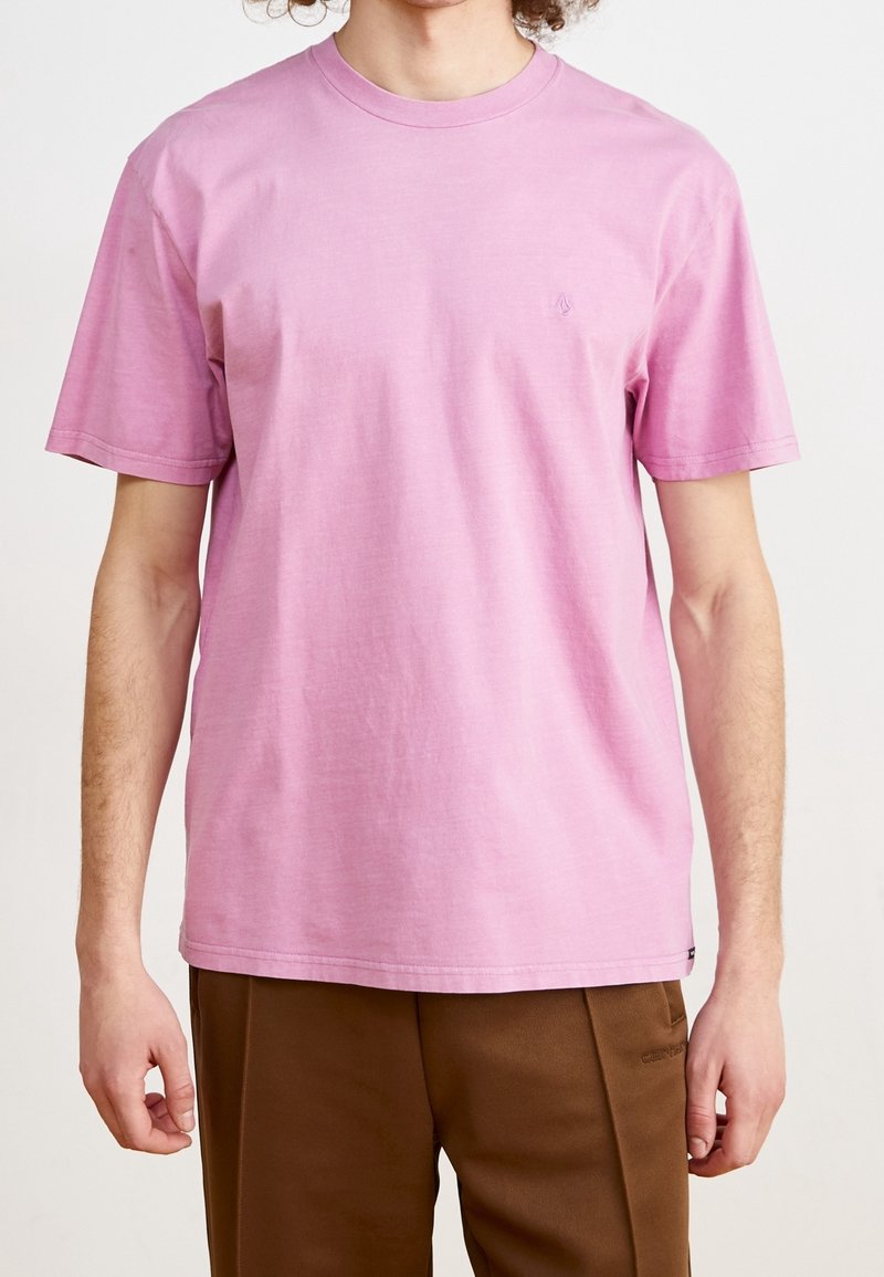 T-shirt à manches courtes, col rond, en coton rose clair avec un petit logo sur la poitrine et une coupe décontractée.