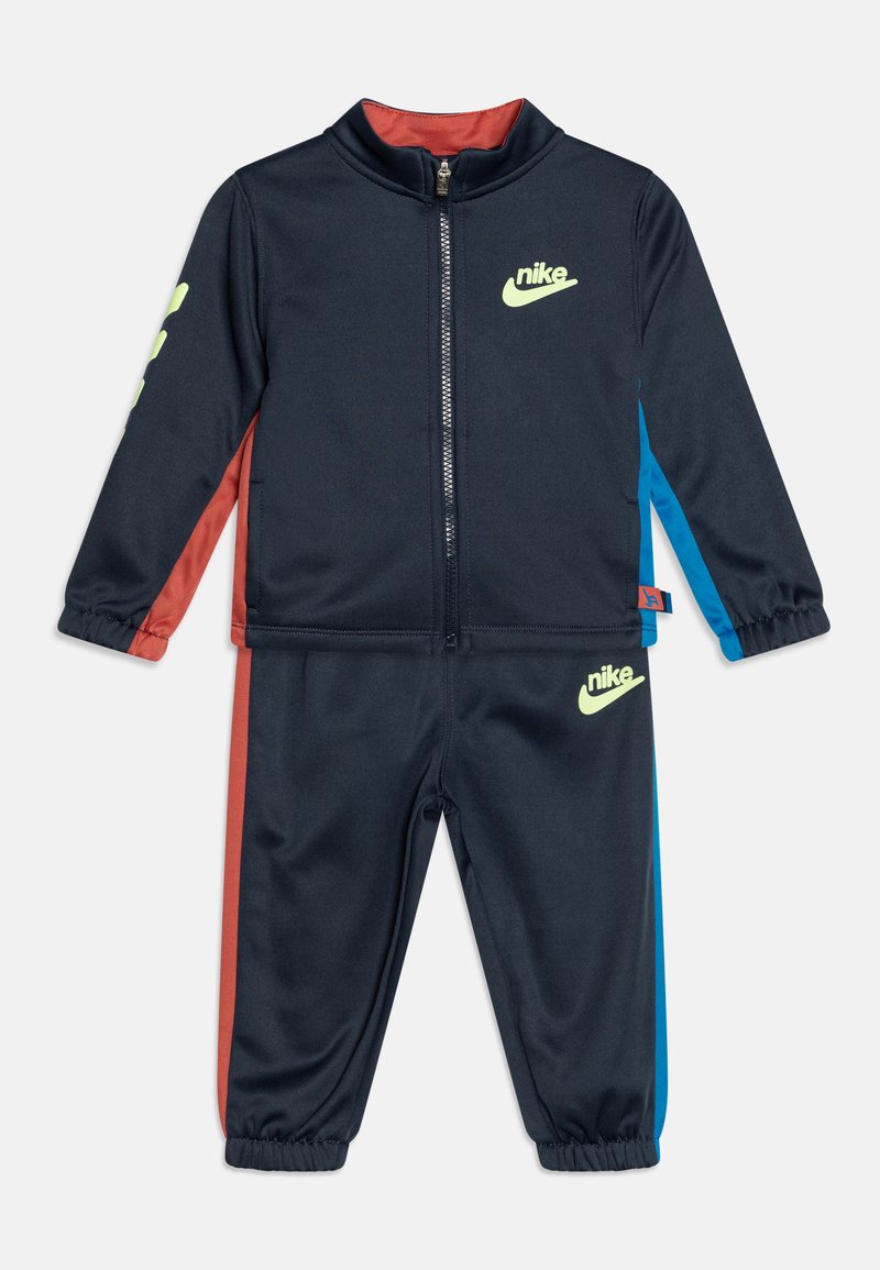 Chándal para niños de Nike en azul marino oscuro con logotipos neón, paneles laterales rojos y azules, puños elásticos y cierre frontal en la chaqueta.