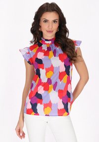 Bluză cu un model tipar, având guler înalt, mâneci scurte în ondulații și un amestec de forme abstracte în nuanțe de roșu, roz, galben și violet pe un fundal deschis.