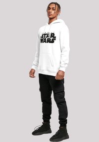 Hvit hettegenser med "STAR WARS"-logo i svart, frontlomme, lange ermer, kombinert med svarte cargo-bukser og svarte joggesko.