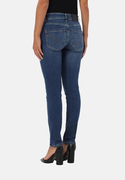 Jean skinny en denim bleu foncé avec une taille moyenne, dotés de poches arrière et de coutures contrastées, associés à des chaussures à talons hauts noires.