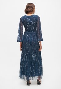 Robe longue bleu marine en tissu transparent ornée de motifs floraux en sequins. Dotée de manches longues et d'une taille cintrée, elle s'étend jusqu'au sol.