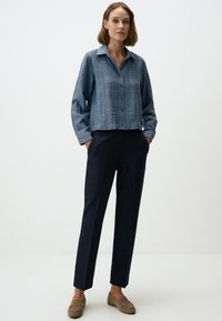 Lichtblauw, textuur shirt met kraag, gecombineerd met donkerblauwe broek en bruine instappers, handen in de zakken, casual fit.