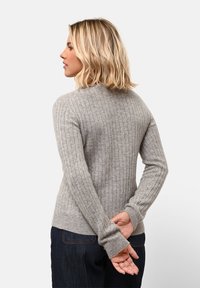 Harmaa ribattu neule korkealla kauluksella ja pitkillä hihoilla. Ominaisuuksiin kuuluu muotonsa ansiosta kapea malli ja pehmeä texture, yhdistettynä tummiin farkkuihin.