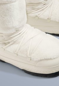 Hvide vinterstøvler med en blanding af blødt fleece og glat læder, med elastiske snørebånd og en tekstureret sort gummisål.