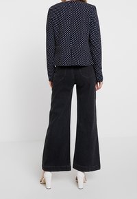 Blazer bleu marine à pois avec manches longues, associé à un jean large noir taille haute et à des sandales blanches à talons.