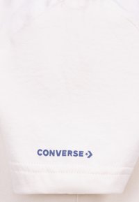 White cotton t-shirt featuring a round neckline and short sleeves. The left sleeve has blue "CONVERSE" text with an arrow accent.