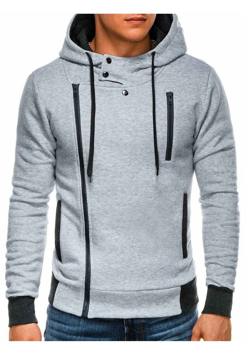 Sweat à capuche gris avec fermeture éclair à l'avant, accents noirs, et capuche à cordon de serrage. Comprend des poches de chaque côté ainsi que des poignets et un ourlet côtelés.