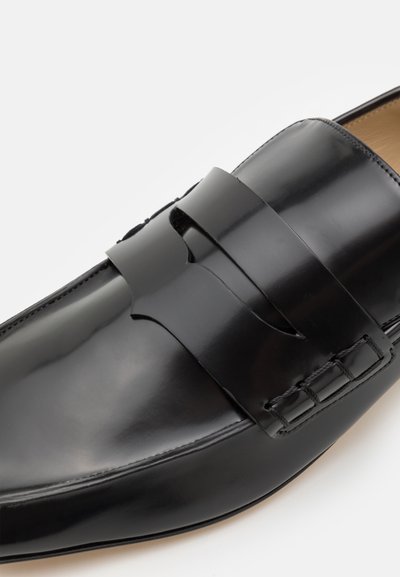 Melnas ādas loafers ar plašu siksnu pāri augšdaļai, ar izšuvumu detaļām gar malu un gludu, spīdīgu apdari.