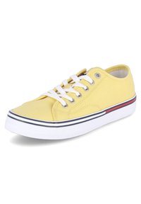 Sneaker giallo in tela con lacci bianchi, suola in gomma e una striscia blu e rossa vicino al fondo. Punta arrotondata e design a taglio basso.