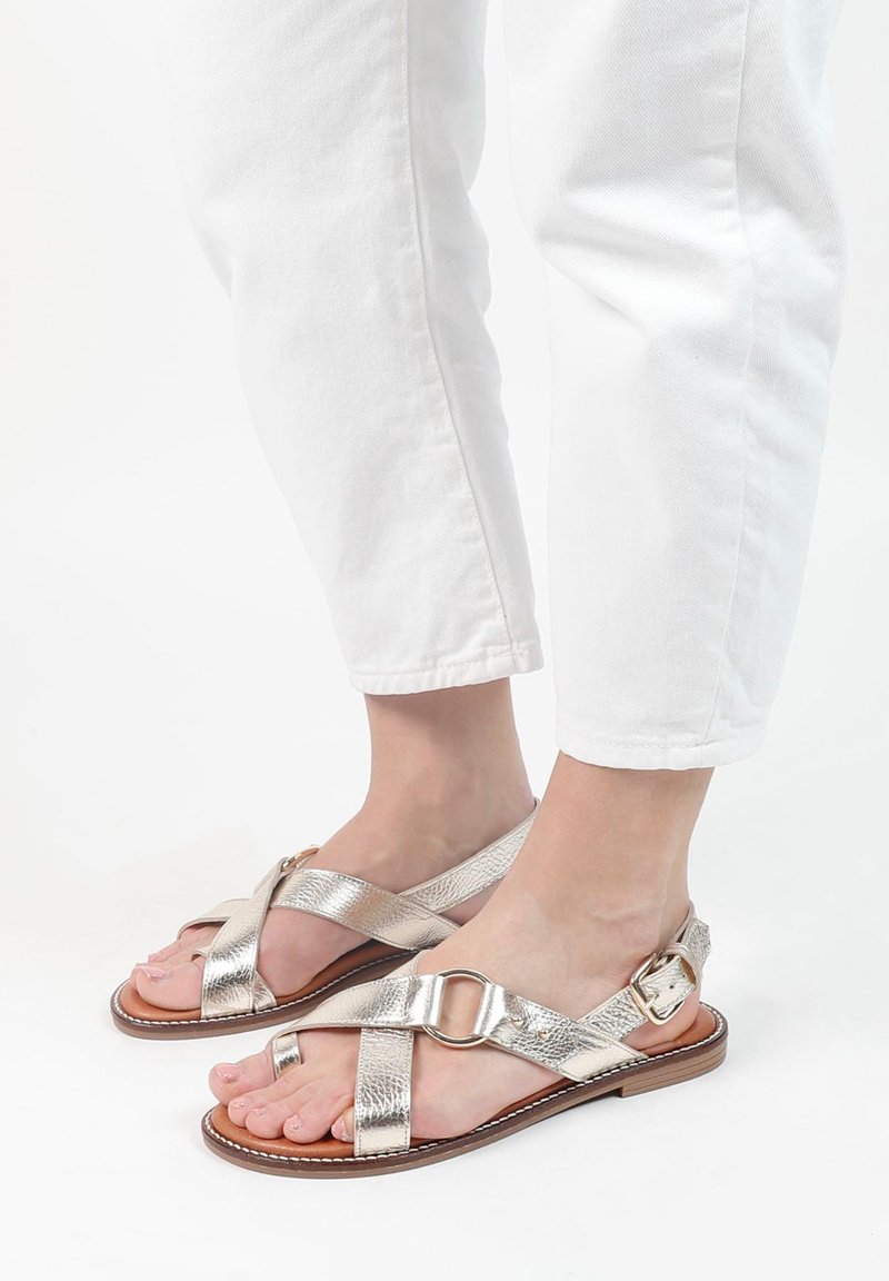 Metallisch zilveren sandalen met kruislings banden en een ronde hardwaredetail. Platte zool met een gestructureerde afwerking, open toe ontwerp.