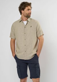 Lys brun kortærmet skjorte med krave, tekstureret stof og brune knapper. Parret med marineblå cargo shorts med sidelommer.