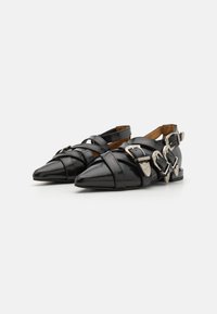 Zapatos de charol negro con punteras puntiagudas, con correas superpuestas y acentos de hebilla plateada. Diseño de tacón plano y parte trasera abierta.