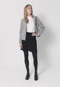 Szara kurtka bomberka na zamek, na białej długiej koszuli, zestawiona z czarną spódnicą i czarnymi legginsami, dopełniona czarnymi botkami za kostkę.