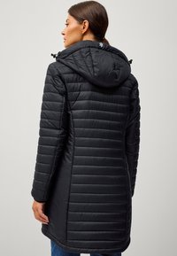 Sort pufferjakke med hætte, der har et quiltet design og struktureret overflade. Justerbare snore i hætten og en længere modellen.