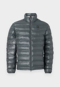 Giacca a vento imbottita di colore grigio scuro, con texture trapuntata, colletto alto, chiusura frontale con zip completa, polsini elasticizzati e un piccolo dettaglio del logo vicino alla parte superiore sul lato sinistro.